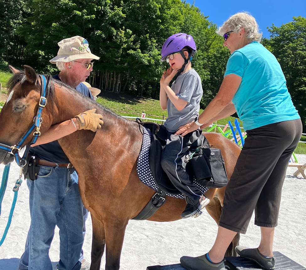 Volunteer assisting a participant brush a horse's tail